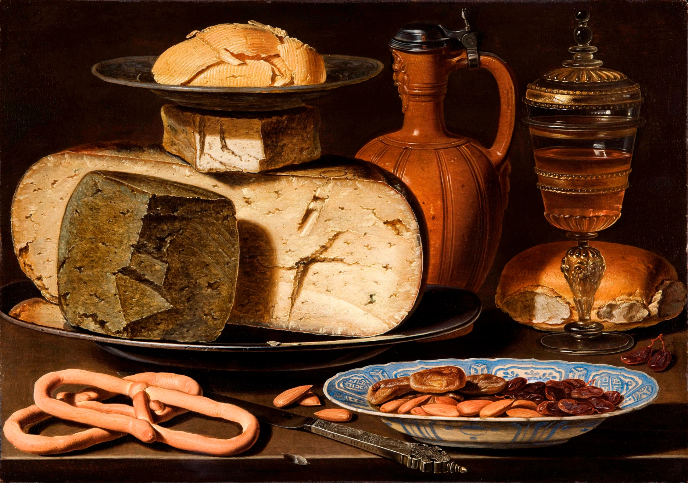 Clara Peeters, Natura morta con formaggi, mandorle e pretzel, 1615 circa, 34,5 × 49,5 cm, Mauritshuis, L'Aia. Il dipinto presenta il coltello firmato e il riflesso della pittrice sul bordo del coperchio della brocca. Opera acquistata dal Mauritshuis nel 2012.